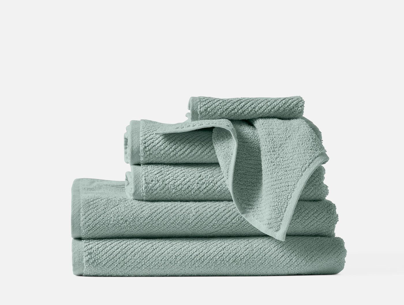 Stacked sage Coyuchi Air Weight towels showing textured weave pattern, various sizes.