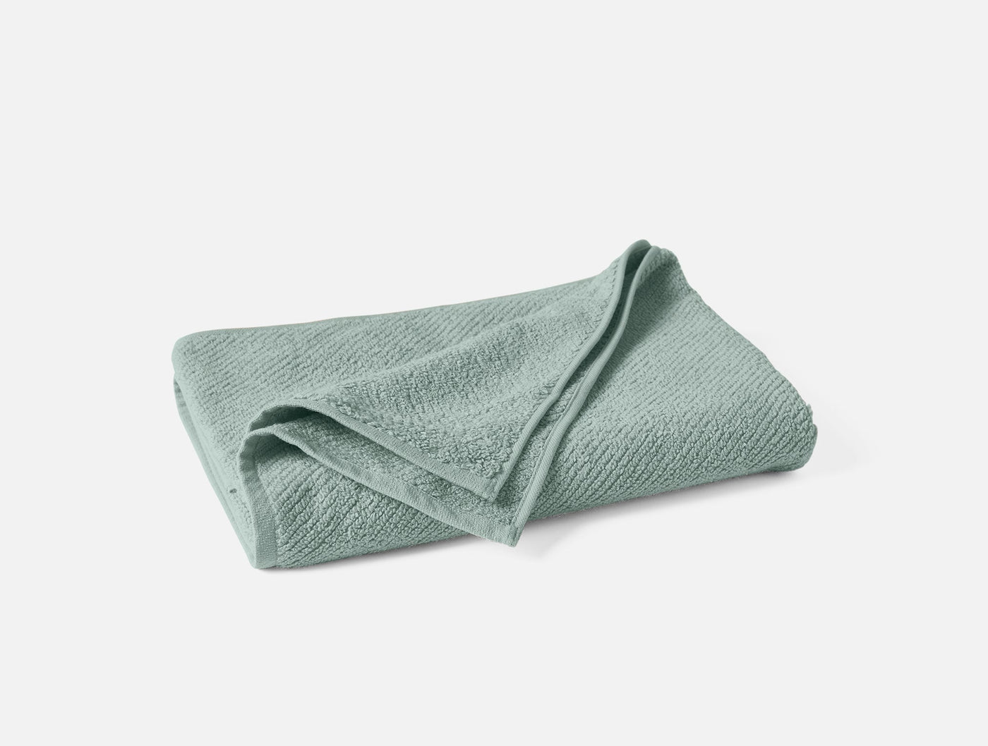 Folded sage green towel showing subtle woven texture and soft drape.