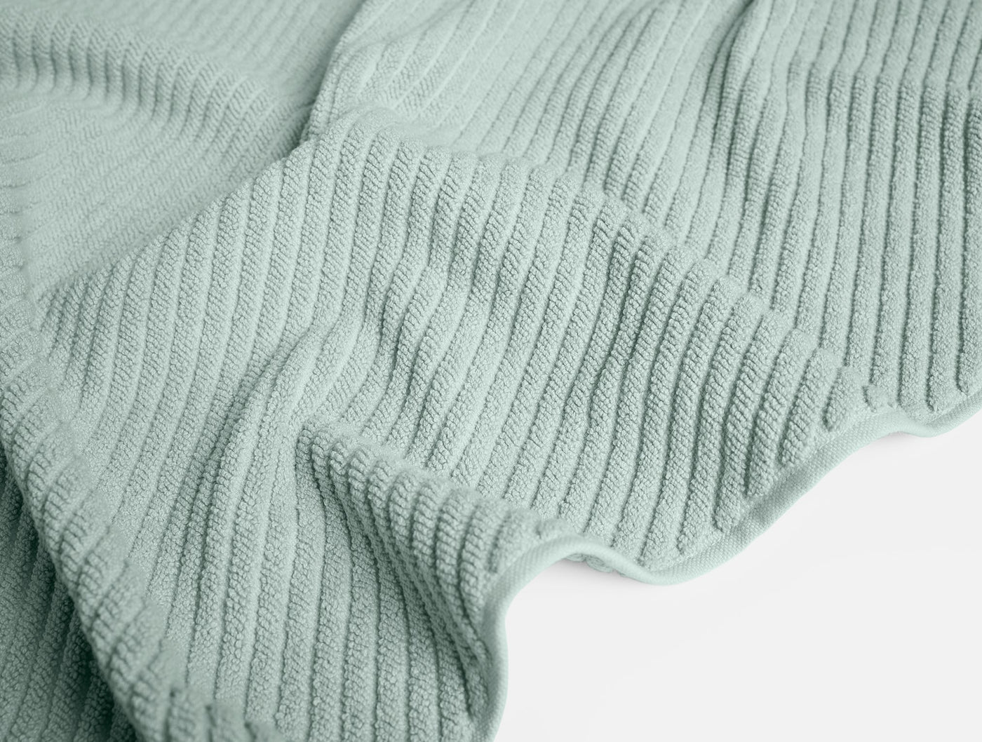 Close-up of Coyuchi Air Weight bath rug in sage, showing ribbed cotton weave texture and scalloped edge.