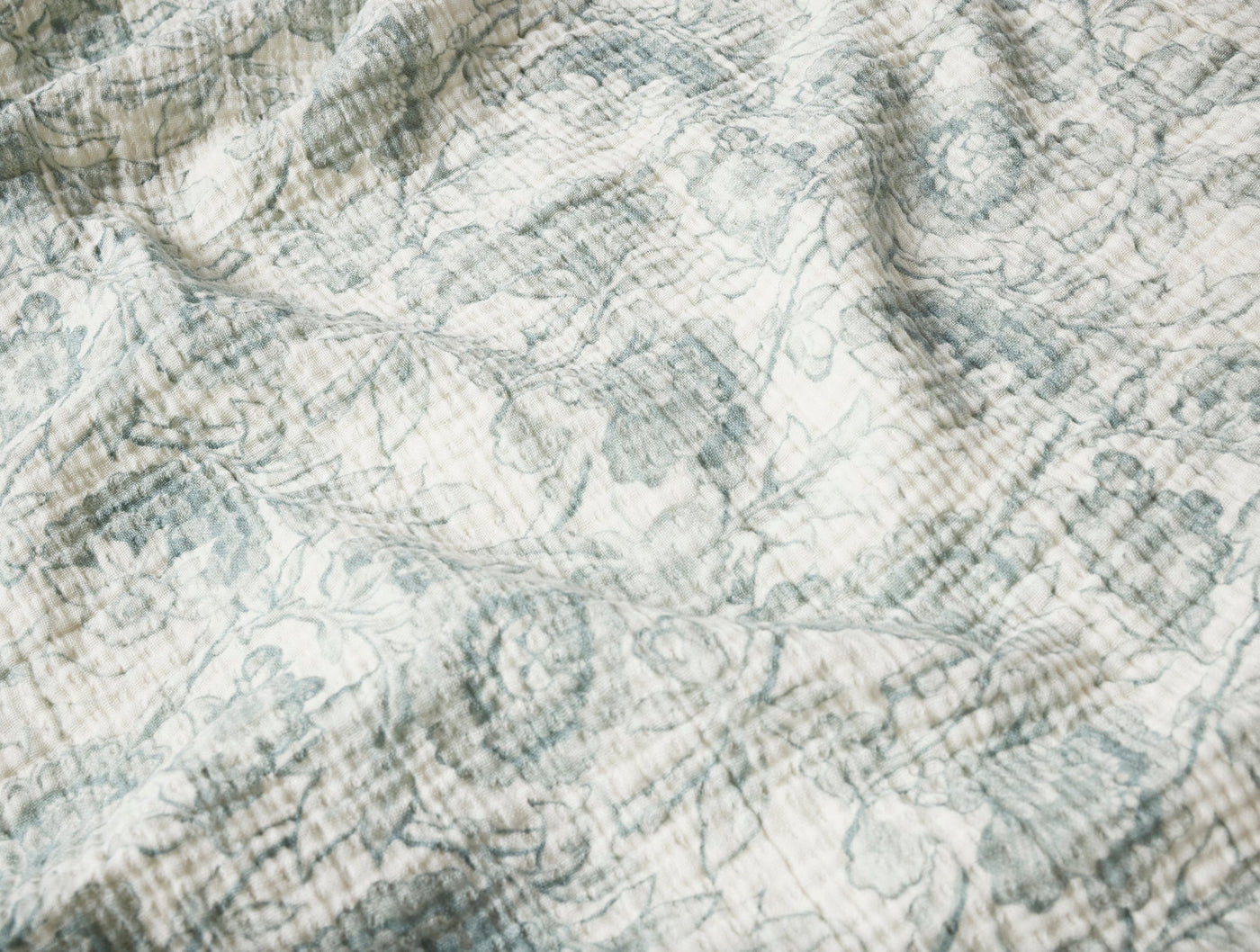 Close-up of Coyuchi Balboa Print throw showing dusty blue floral pattern on ivory textured fabric.