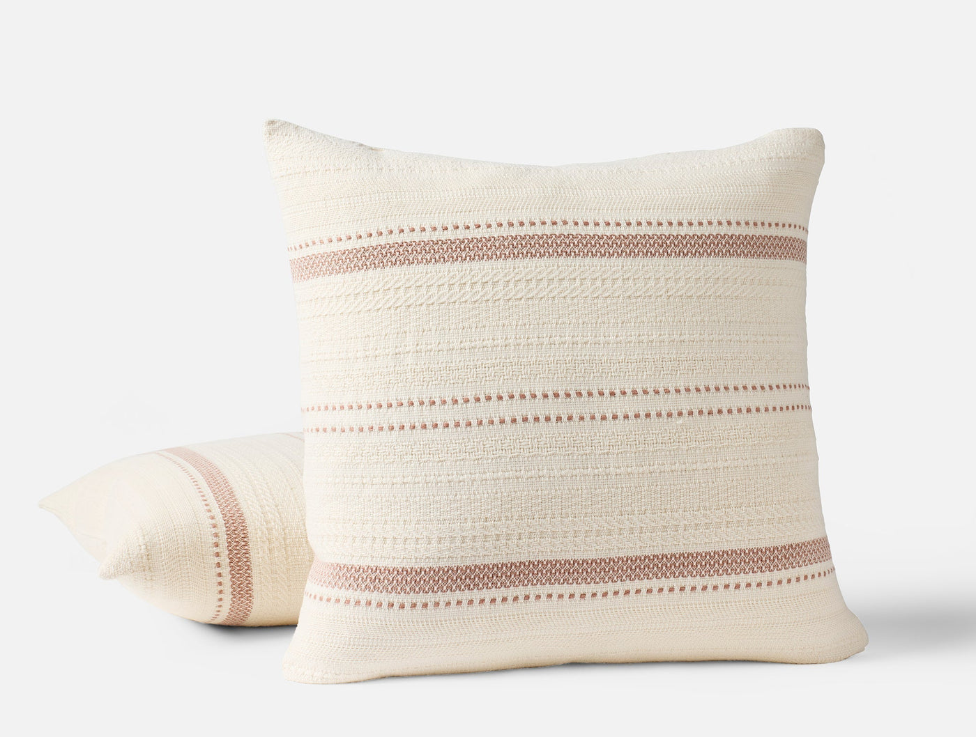 Two Coyuchi Bonita pillows stacked, ivory cotton with dusty rose woven stripe detail.