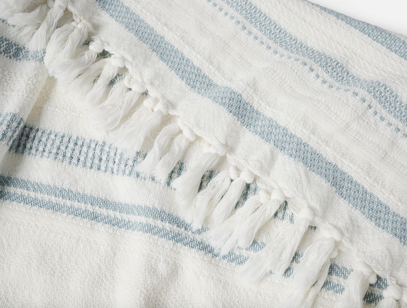 Close-up of ivory and mist blue striped woven throw with knotted fringe detail.