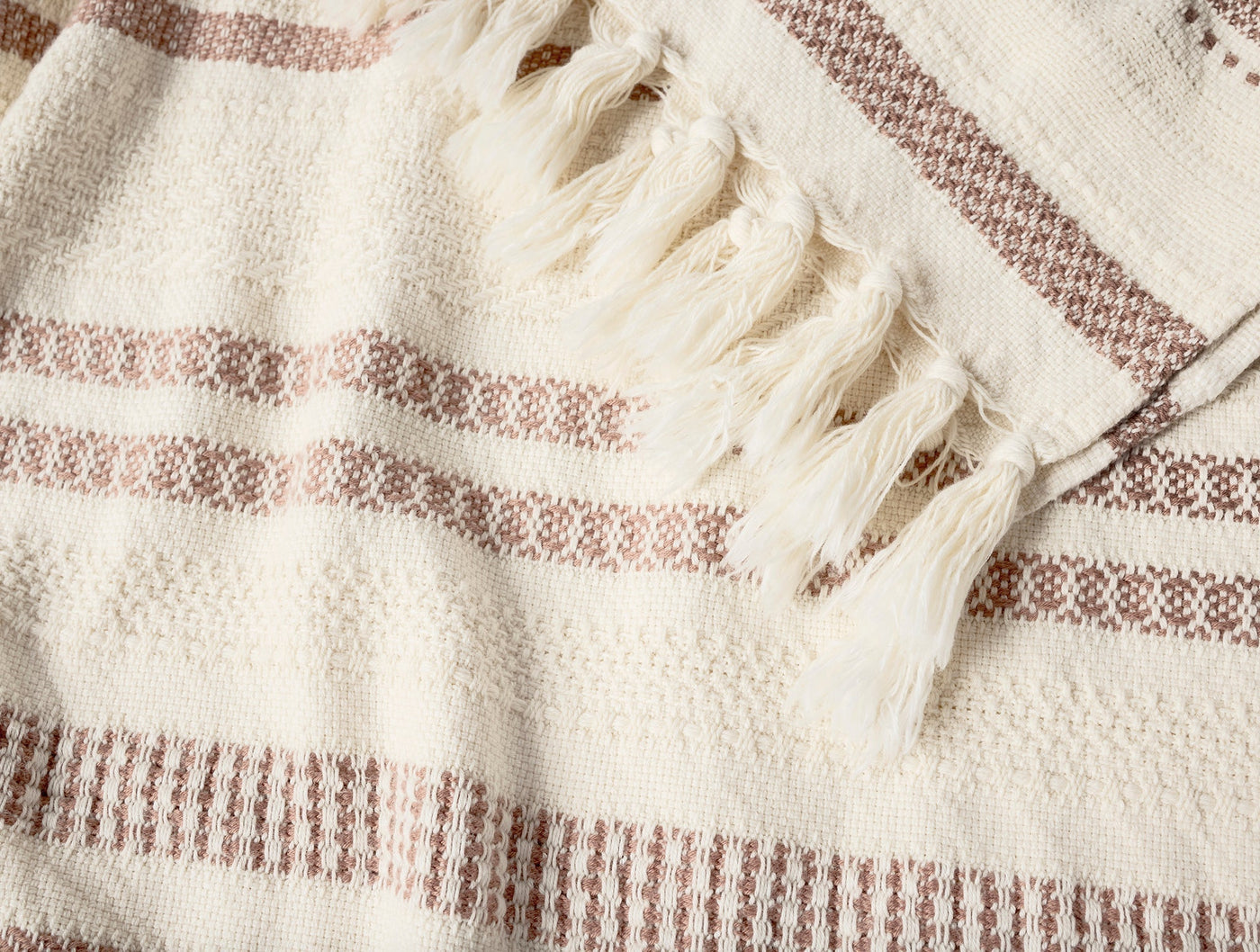Close-up of Coyuchi Bonita throw fringe and dusty rose stripe weave detail on ivory cotton.