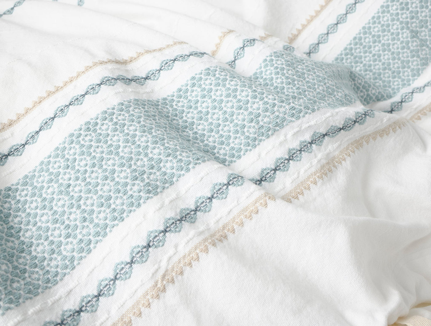 Close-up of Coyuchi Cabrillo duvet cover hem, sage geometric stripes with champagne lacework detail.