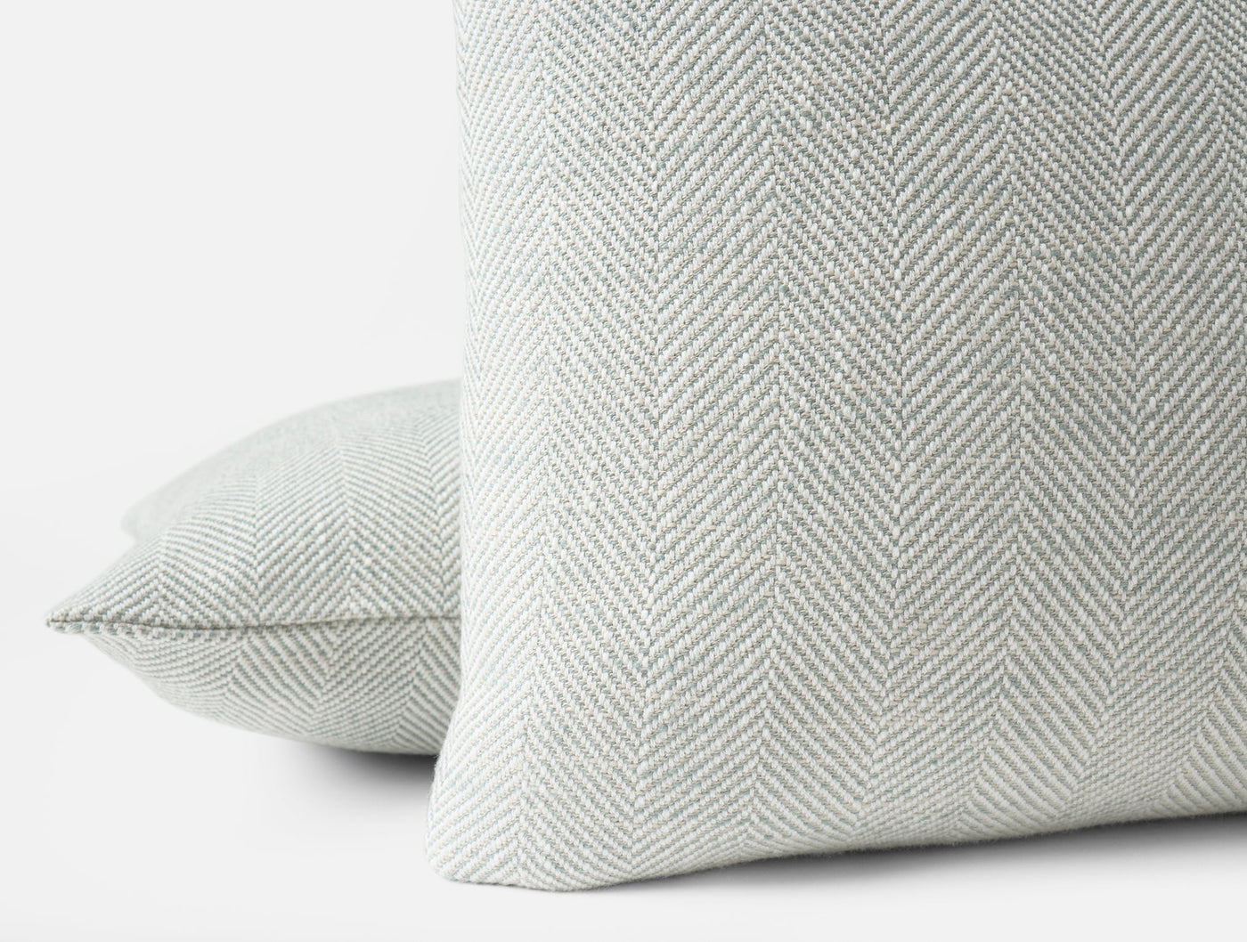 Close-up of Coyuchi Canyon pillow's sage herringbone weave texture, two pillows stacked.