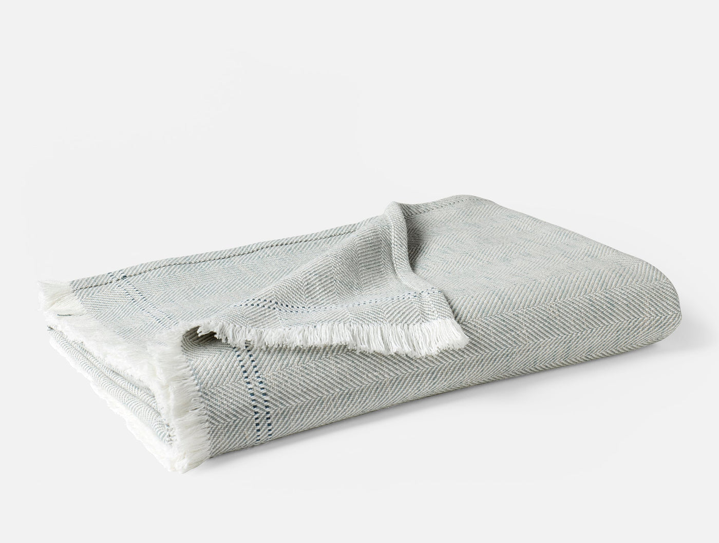 Folded Coyuchi Canyon throw in pale sage, showing fringe trim and herringbone weave texture.