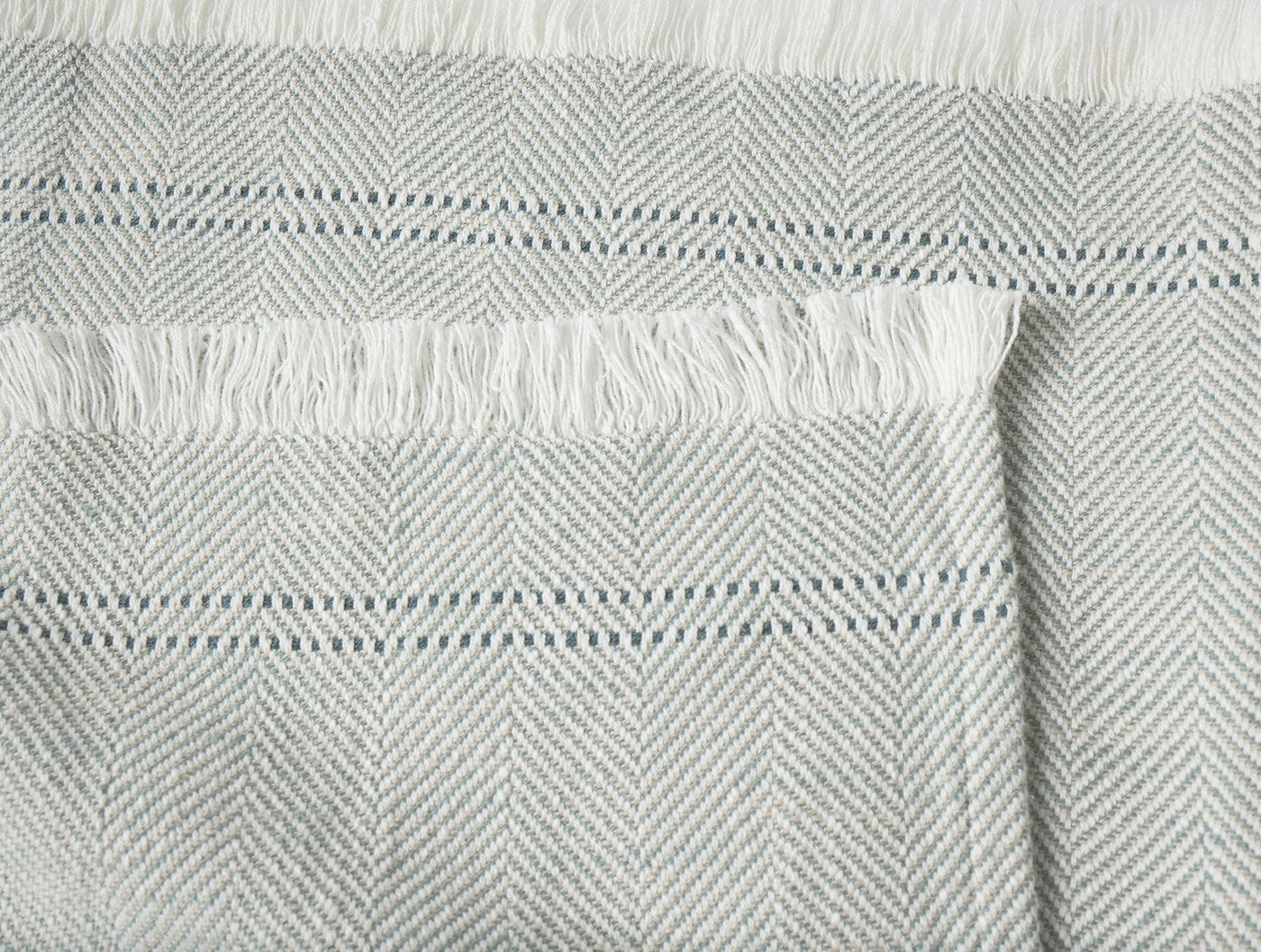 Close-up of Coyuchi Canyon throw fringe edge, showing herringbone weave in soft grey.