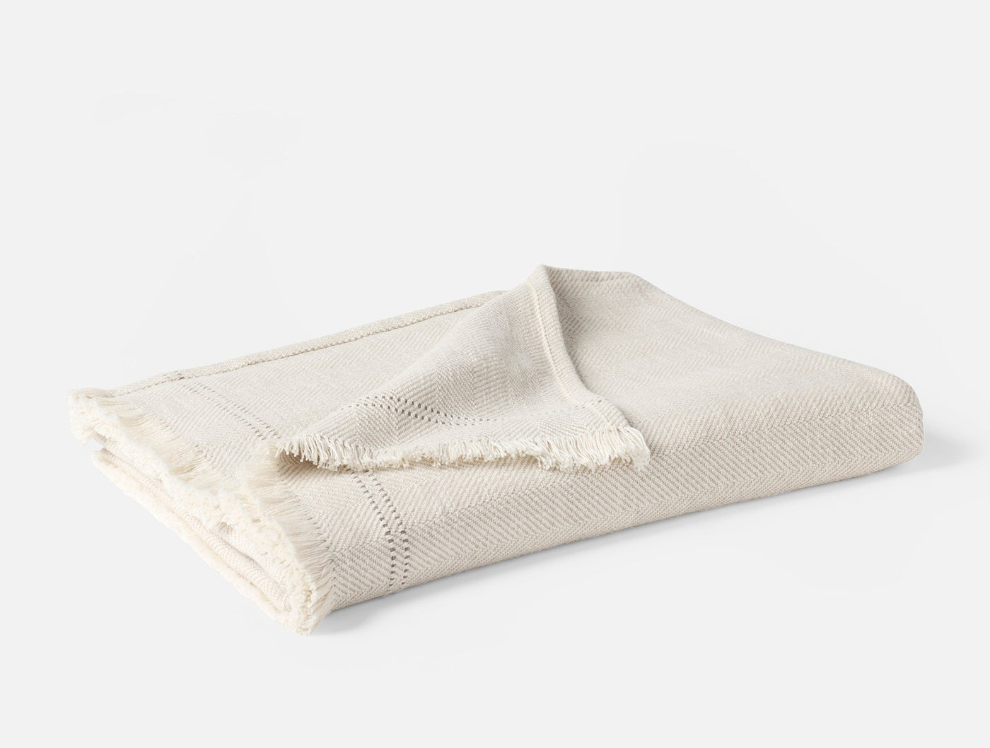 Folded ivory Coyuchi Canyon throw with fringe trim and open-weave texture detail.