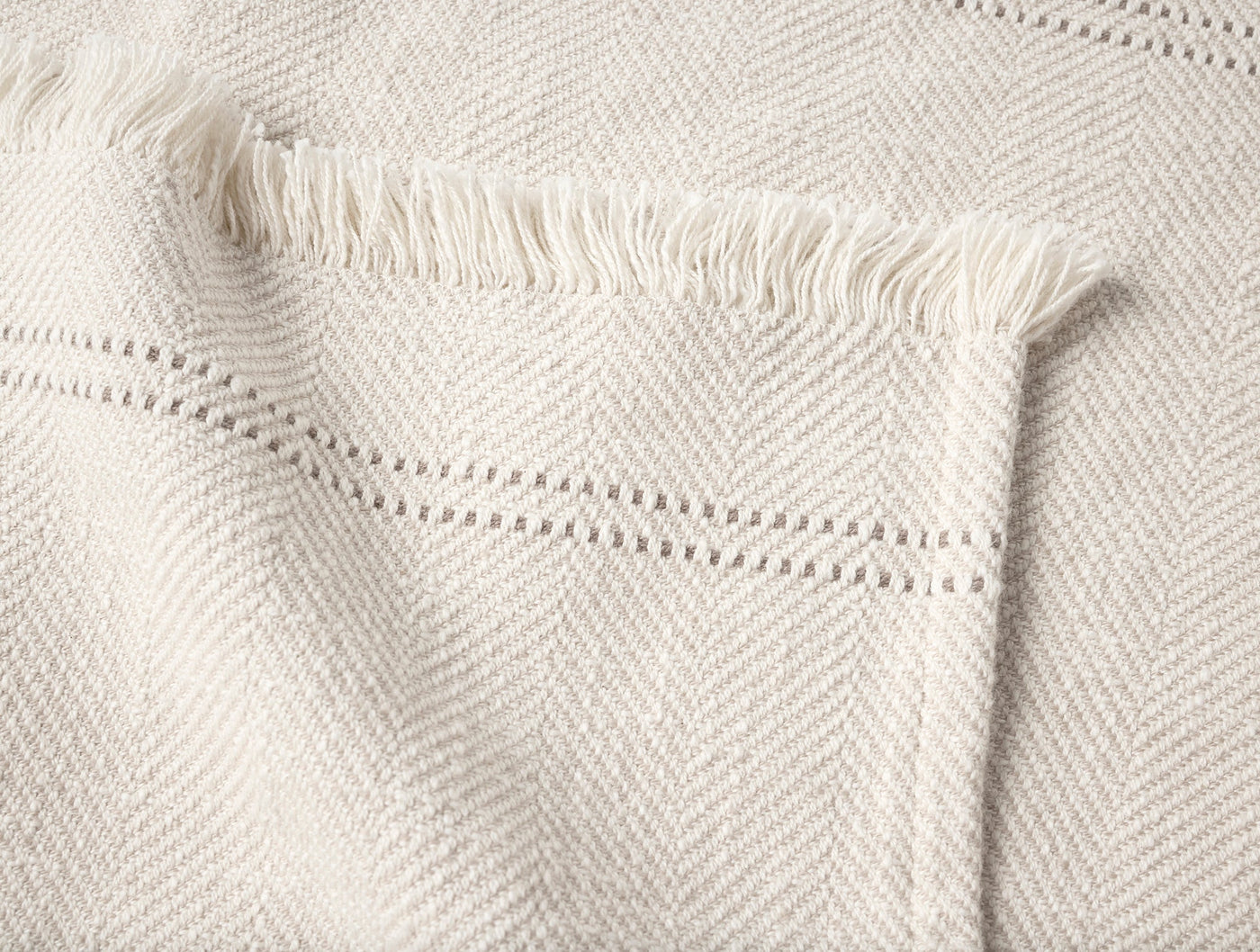 Close-up of ivory herringbone weave throw with fringe edge and ladder hem detail.