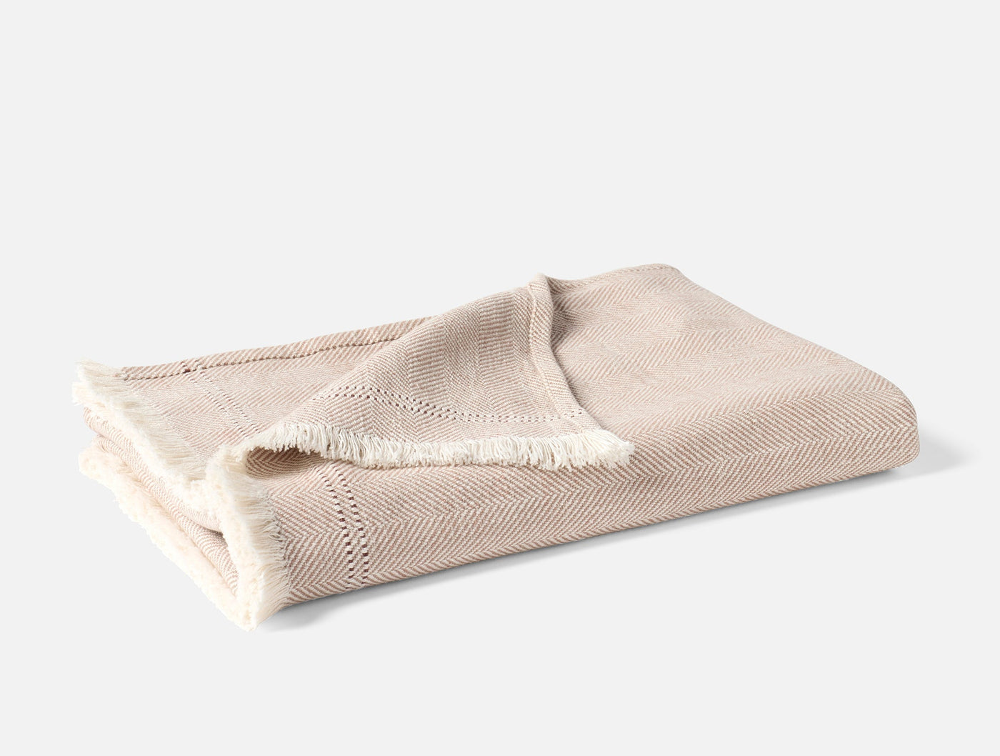 Folded Coyuchi Canyon throw in oatmeal herringbone weave with fringe trim detail.