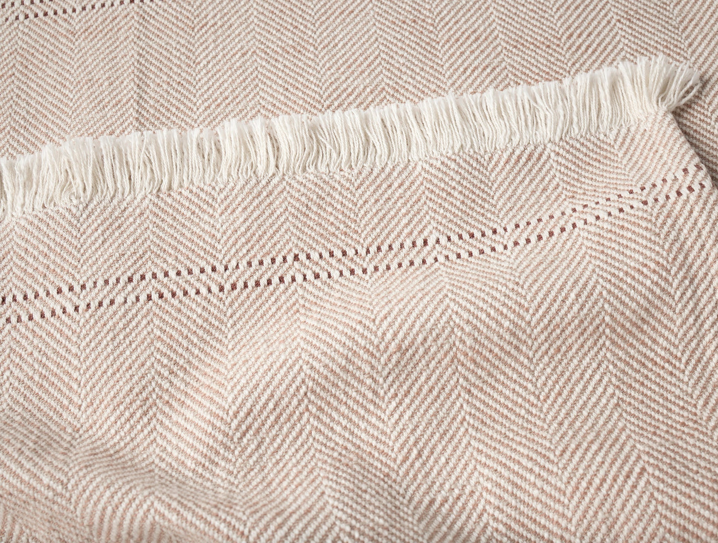 Close-up of Coyuchi Canyon throw fringe edge and herringbone weave in warm sand.