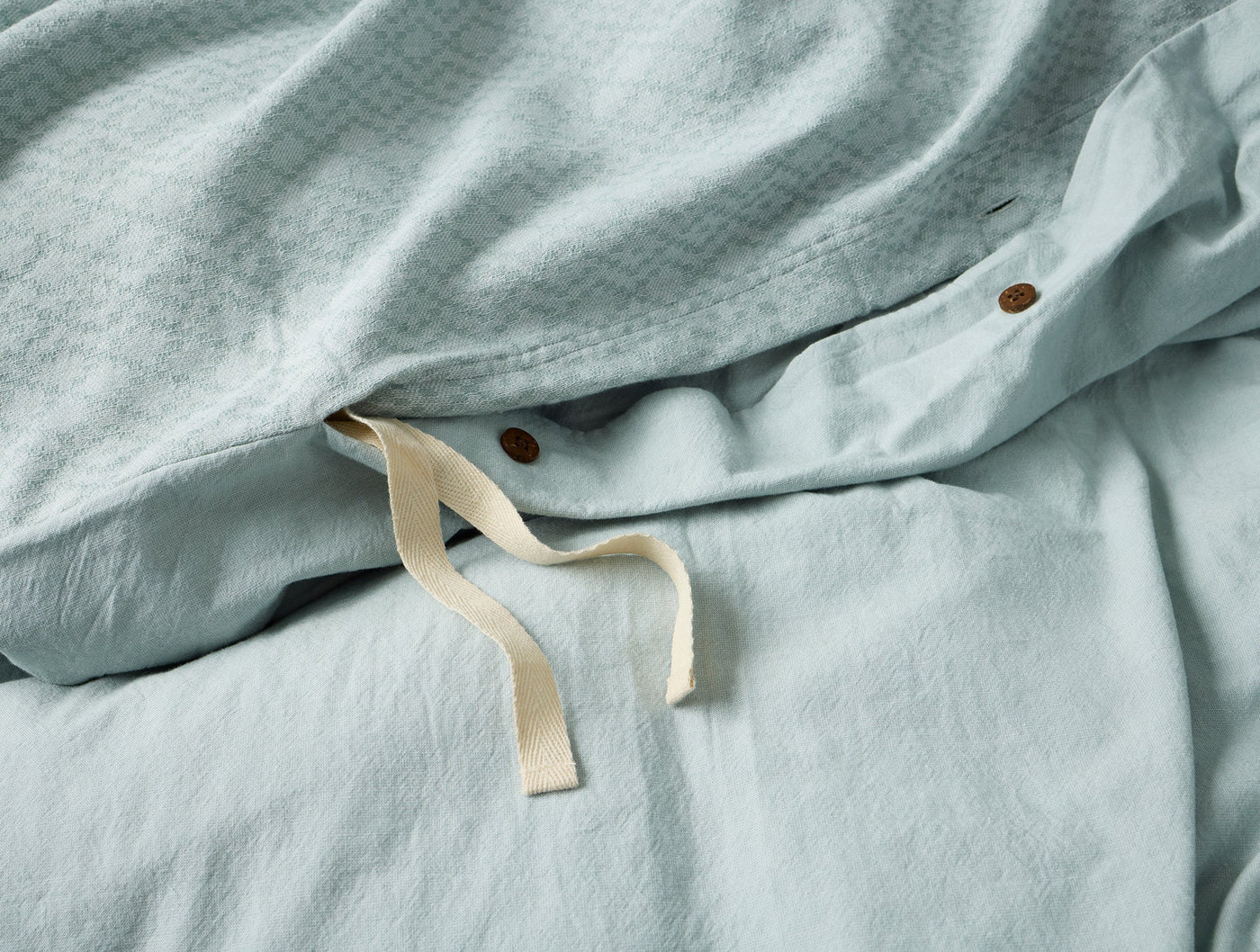 Close-up of Coyuchi Capitola duvet cover interior corner, showing ivory tie and copper snap closure.