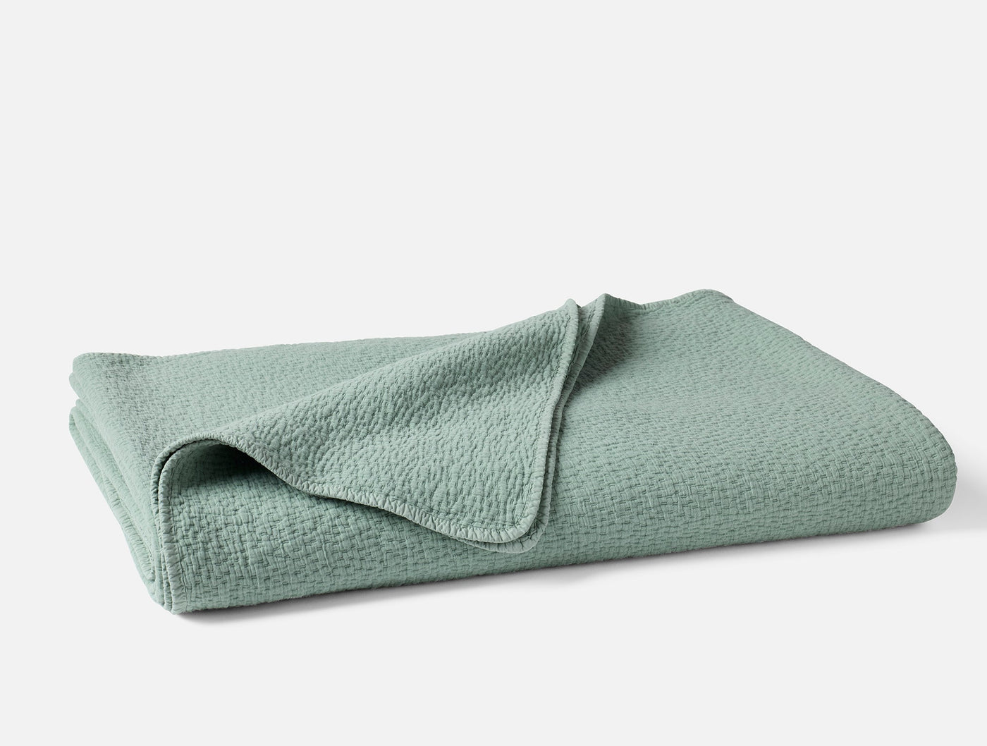 Coyuchi Cascade Matelassé blanket folded, seafoam green with textured weave detail.