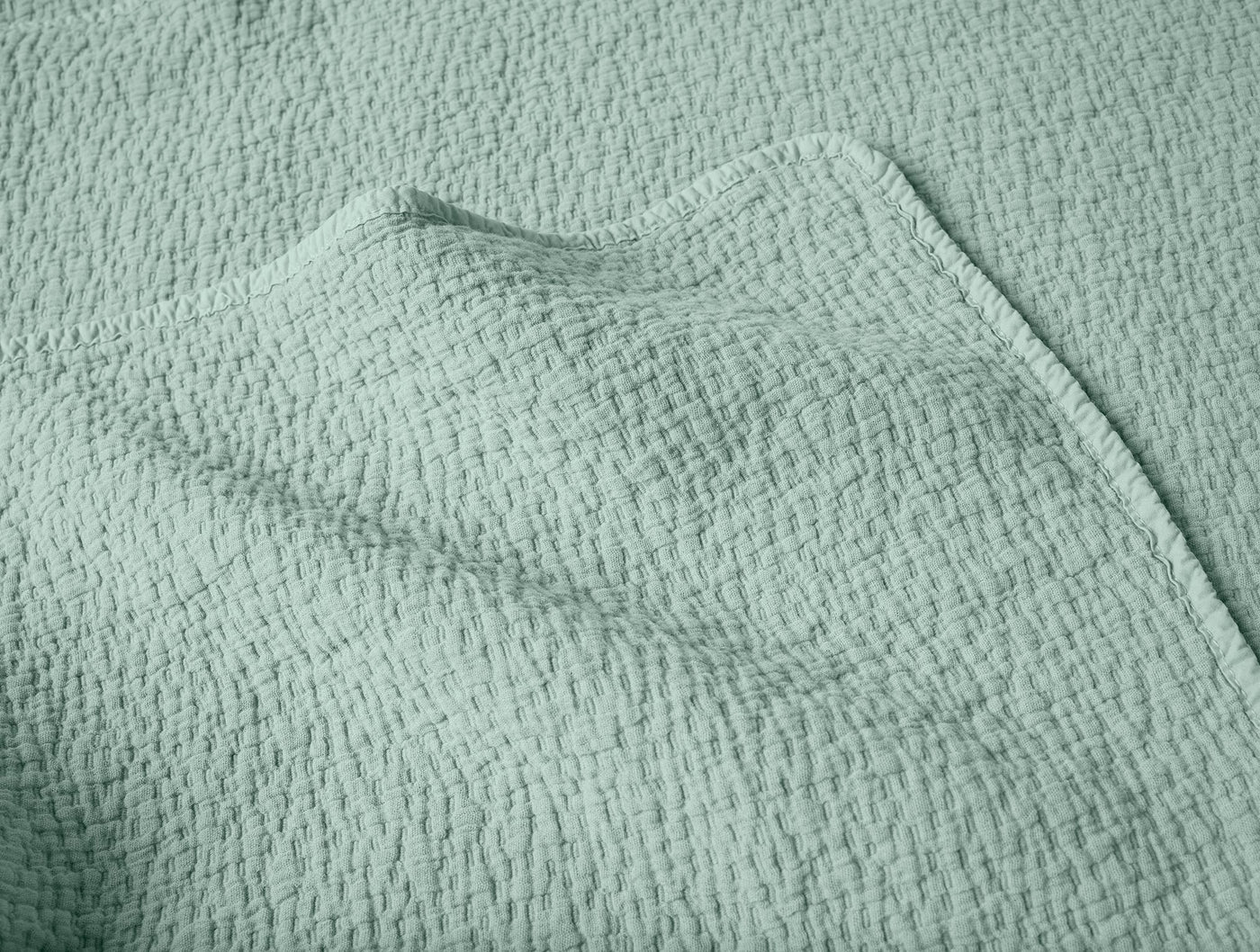 Close-up of Coyuchi Cascade Matelassé blanket in sage, showing textured weave and folded corner.