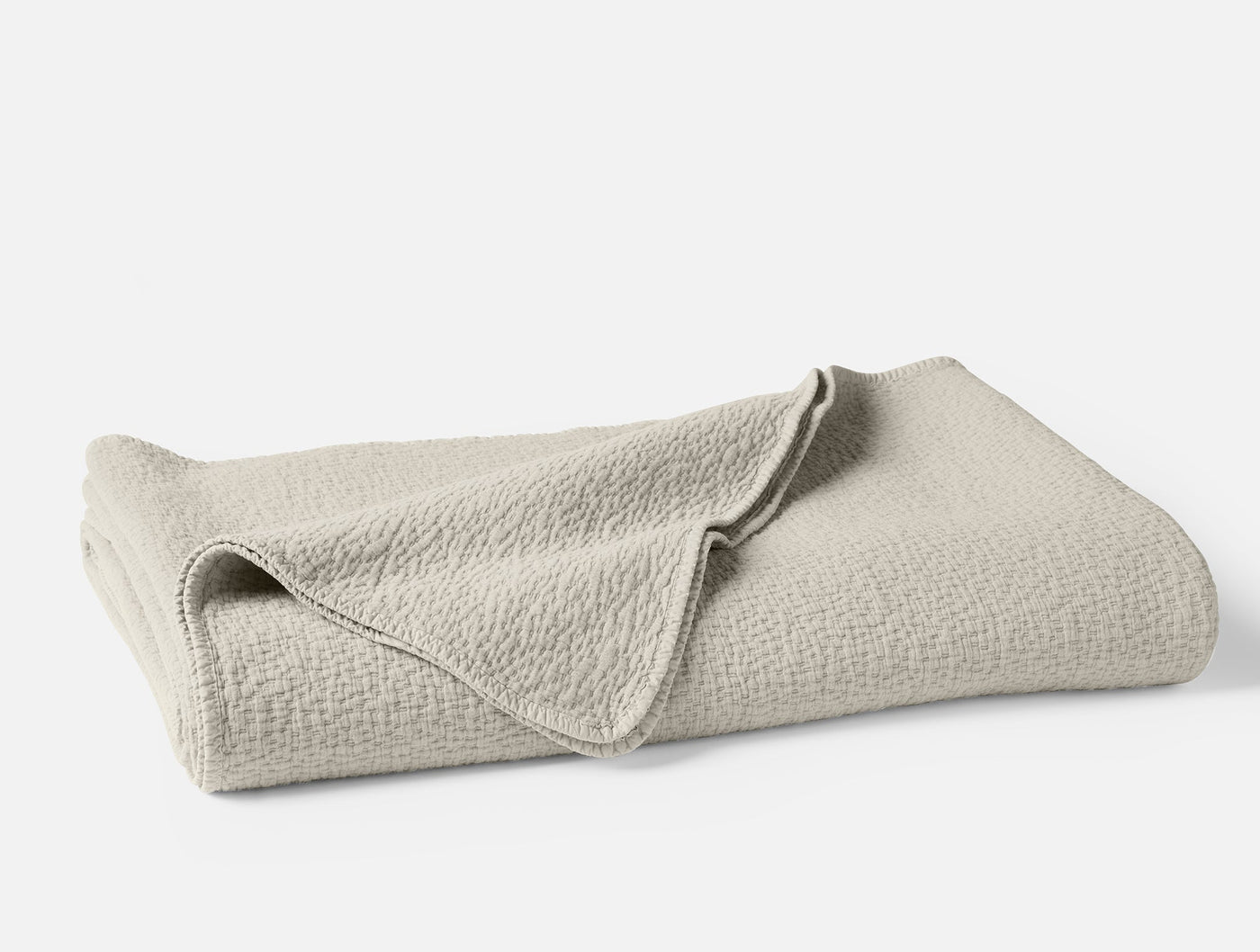 Folded ivory Coyuchi Cascade Matelasse blanket showing textured weave detail.