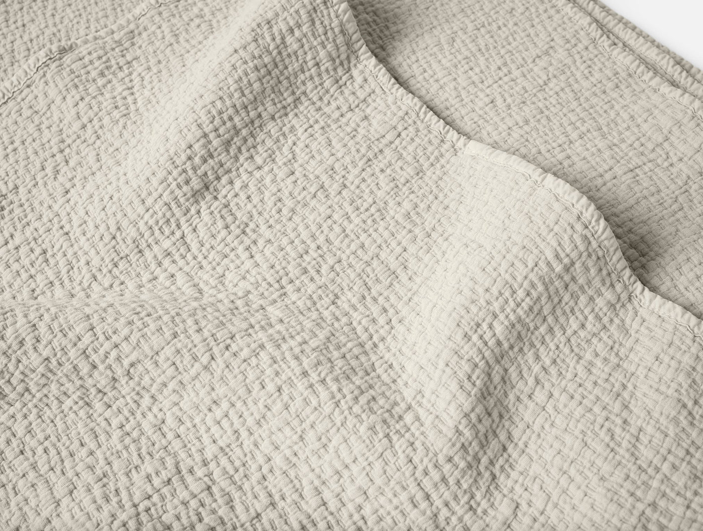 Close-up of Coyuchi Cascade Matelasse blanket showing ivory woven texture and folded edge.