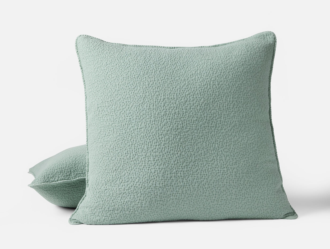Sage green matelassé pillow sham with subtle textured surface, shown with stacked second sham.