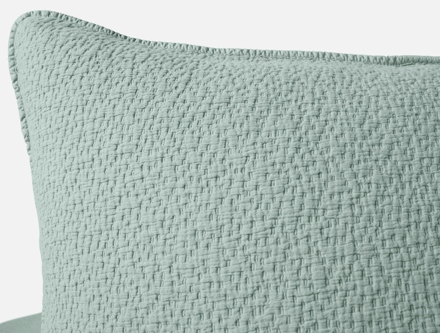 Close-up of Coyuchi Cascade Matelassé sham corner in sage, showing woven texture and whipstitch edge.