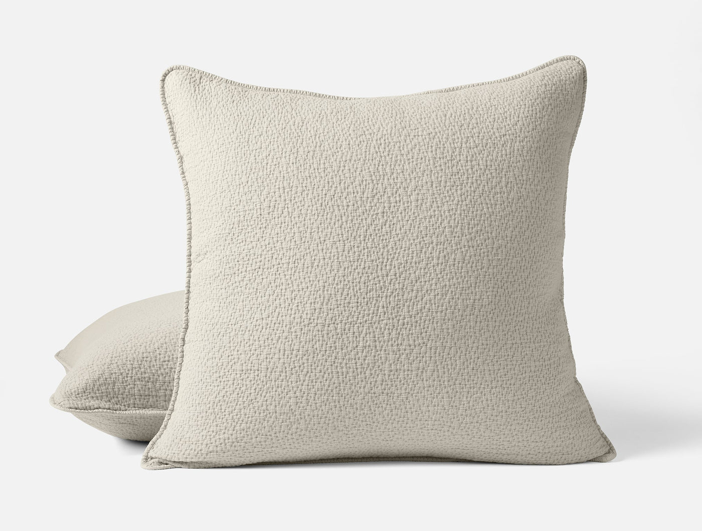 Close-up of two ivory Coyuchi Cascade Matelasse shams with textured boucle weave and corded trim.