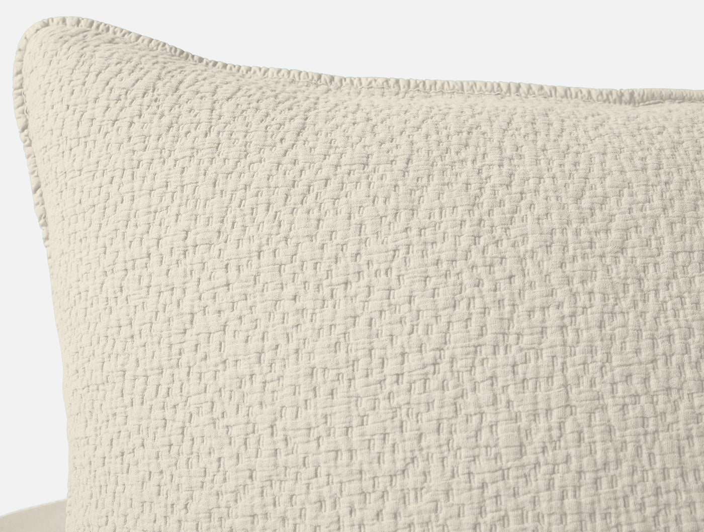Close-up of ivory Coyuchi Cascade Matelasse sham showing woven texture and blanket-stitched edge.