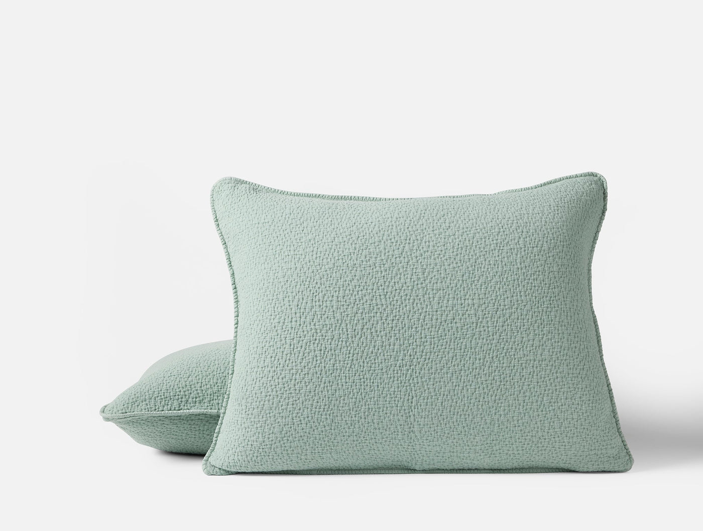 Two Coyuchi Cascade Matelassé shams in sage, showing textured boucle-like weave and piped edges.