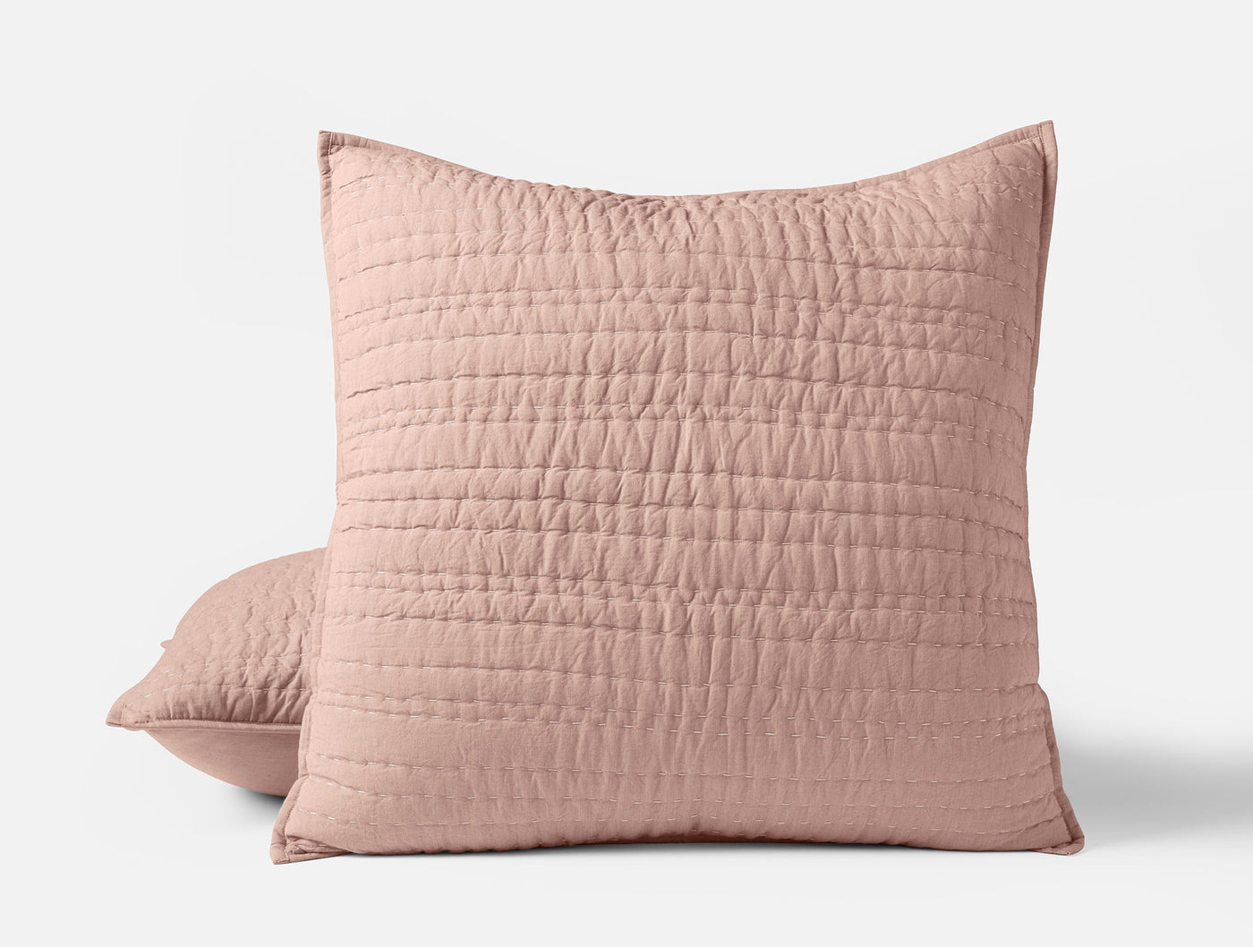 Blush pink quilted pillow shams with channel hand-stitching, stacked pair on white background.