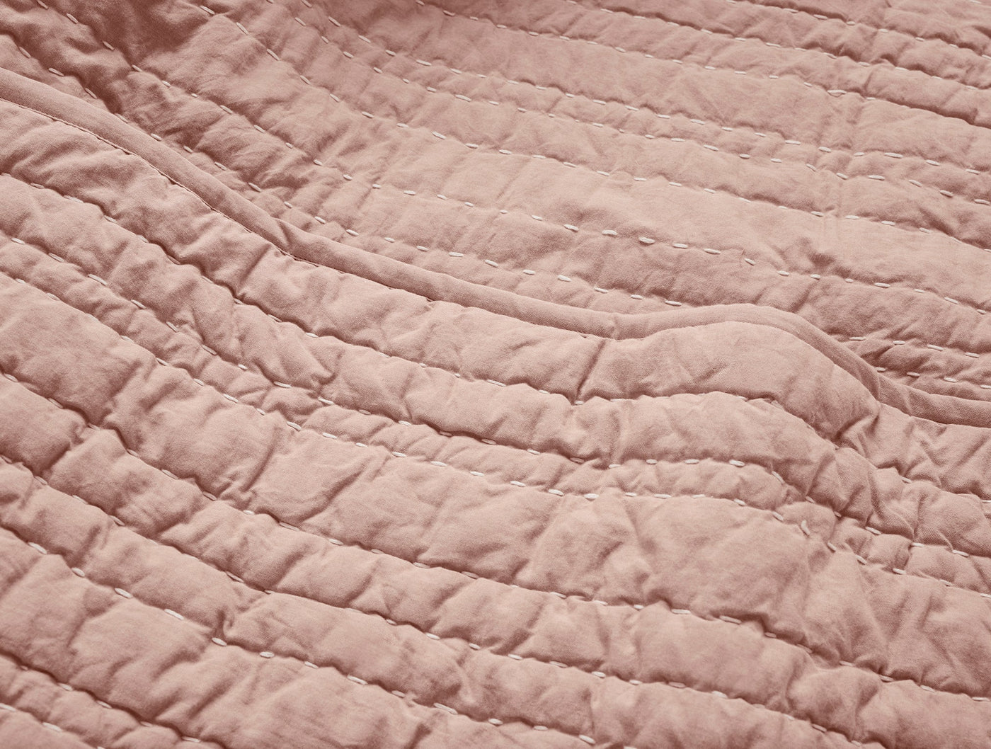 Close-up of blush Coyuchi Channel Handstitched quilt showing parallel stitched rows and texture.