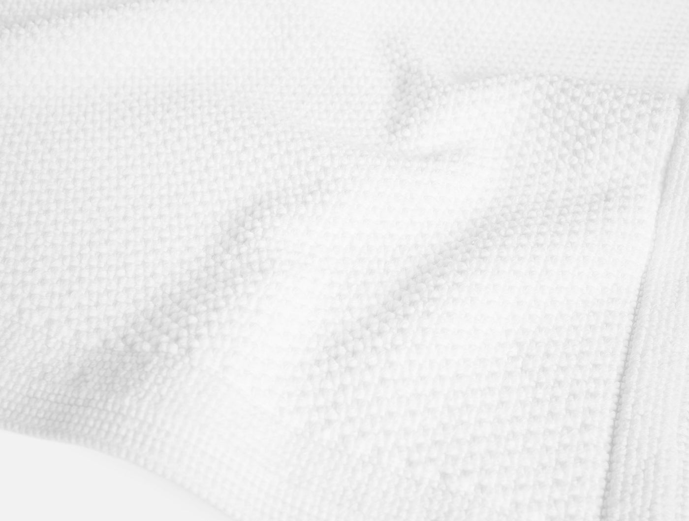 Close-up of Coyuchi Cove bath rug showing white waffle-weave texture and soft drape.