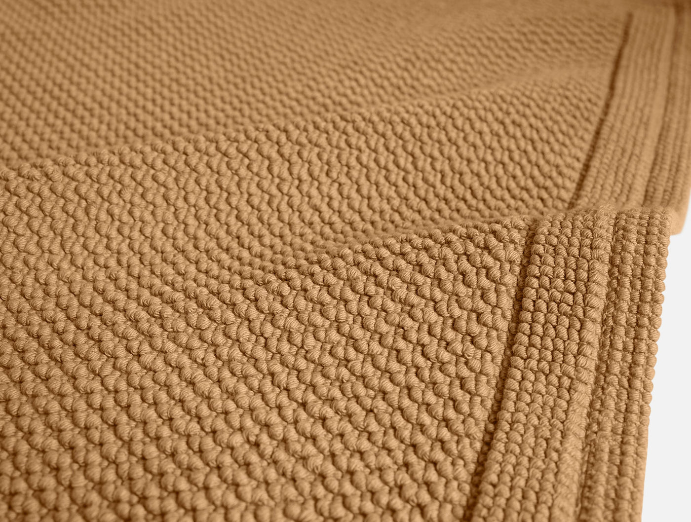 Close-up of Coyuchi Cove bath rug in camel, showing nubby cotton texture and border detail.