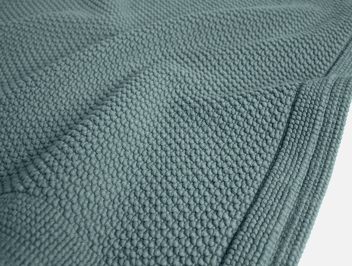 Close-up of Coyuchi Cove bath rug in teal, showing nubby cotton weave texture and hemmed edge.