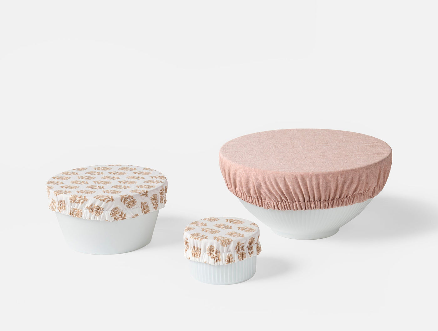 Coyuchi Conserve bowl cover set in blush and floral print, three sizes on white bowls.