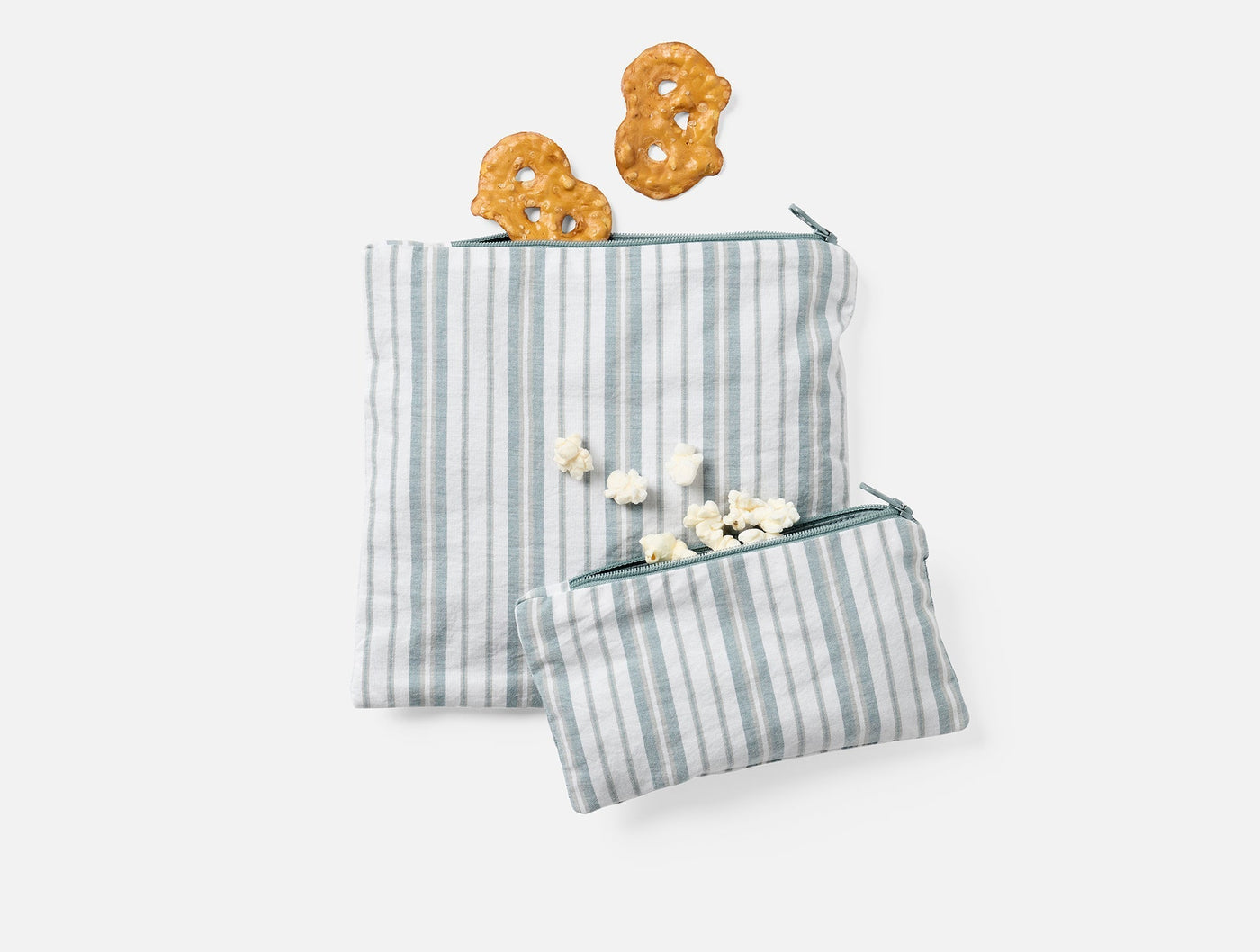 Two sage-striped Coyuchi snack bags styled with pretzels and popcorn, small and large sizes.