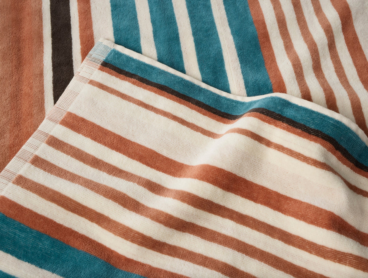 Close-up of folded Coyuchi Dawn Stripe beach towel showing teal, terracotta, and ivory stripe detail.
