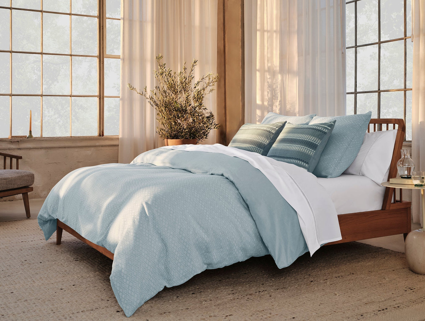 Coyuchi Lattice Percale bedding styled in soft blue on a mid-century wood bed, natural light setting.