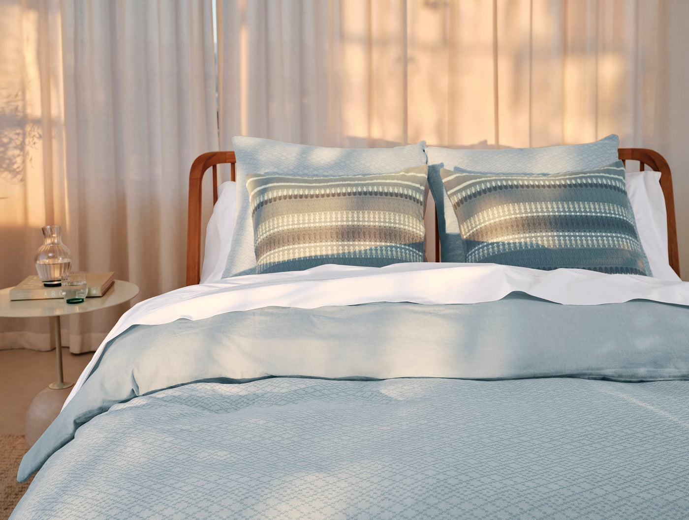 Coyuchi Capitola duvet cover in pale blue, styled on a bed with striped accent pillows.