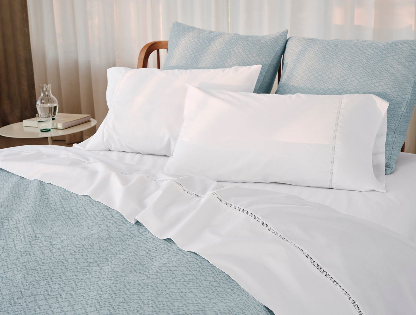 Coyuchi Lattice Percale pillowcases in white, styled on a made bed with blue quilted bedding.