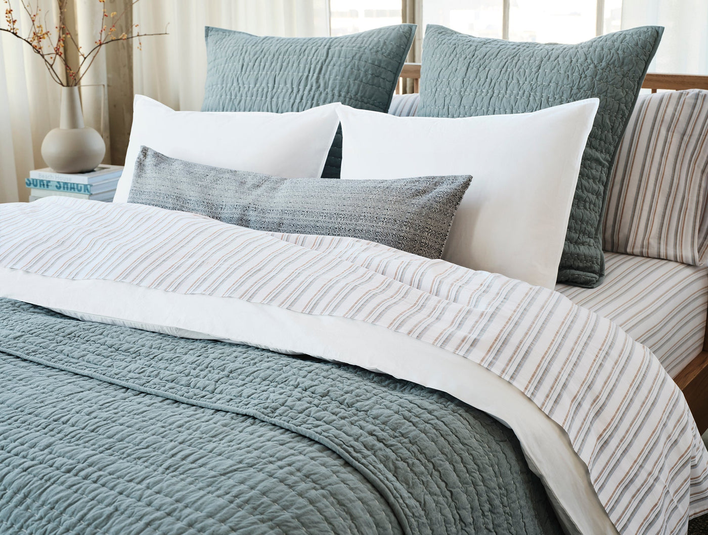 Striped percale duvet peek beneath sage matelassé quilt in a styled bedroom layering.