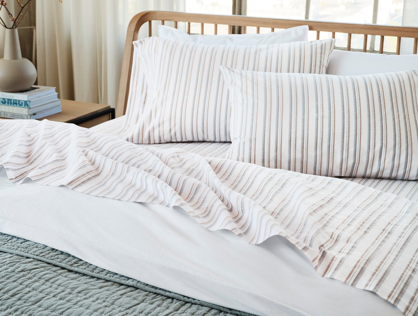 Crinkled percale pillowcases in taupe stripe draped on a styled bed with natural wood frame.