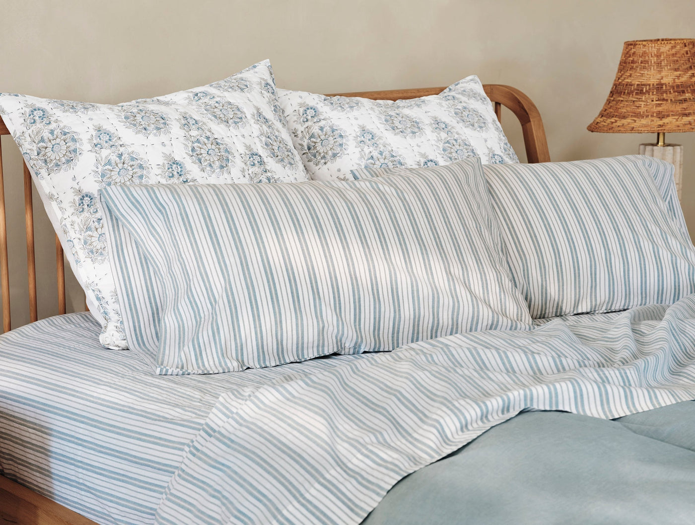 Blue and white striped crinkled percale pillowcases styled on a made bed with floral shams.