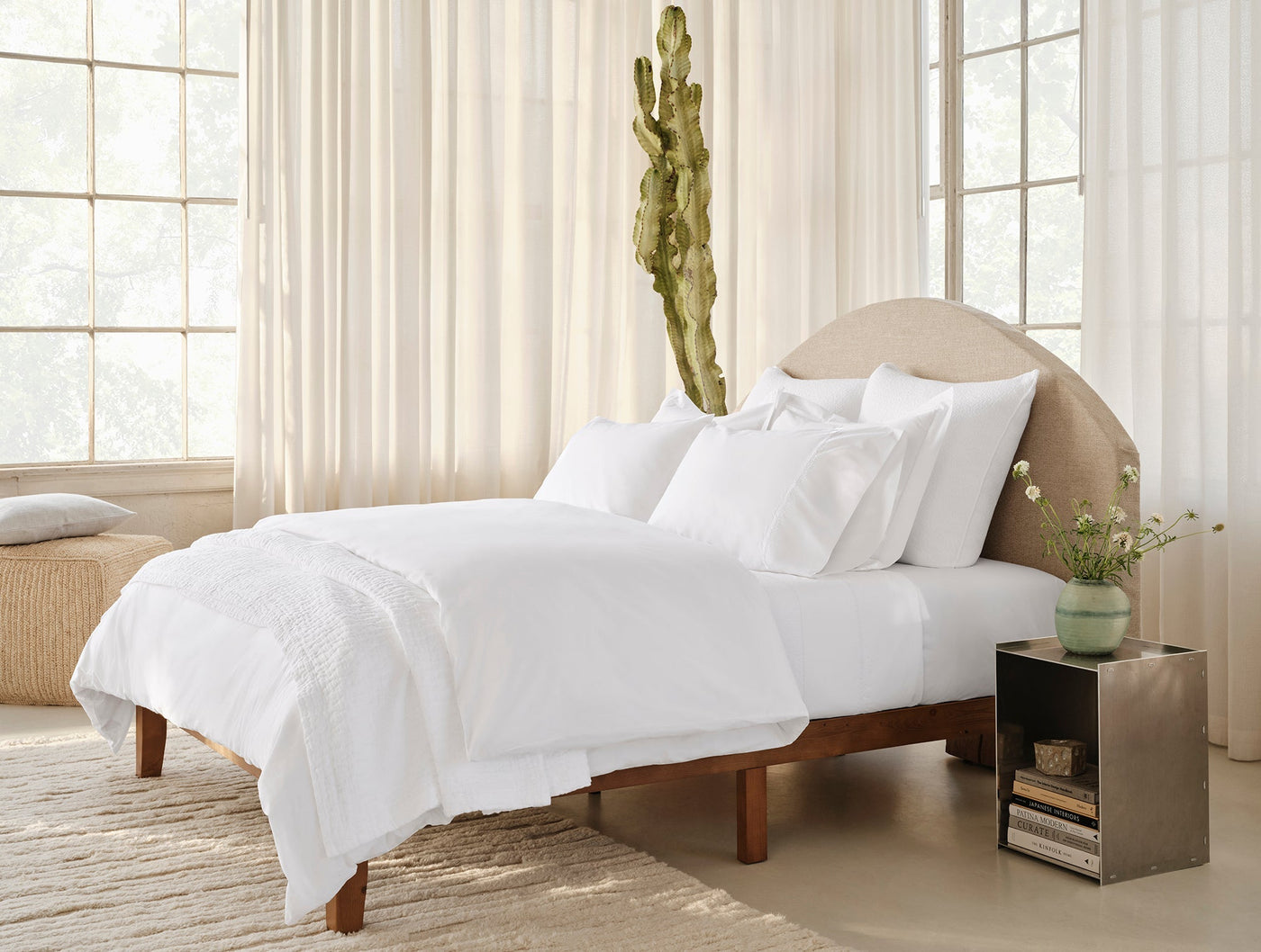 White embroidered sheet set styled on a bed with arched linen headboard, bright airy bedroom.