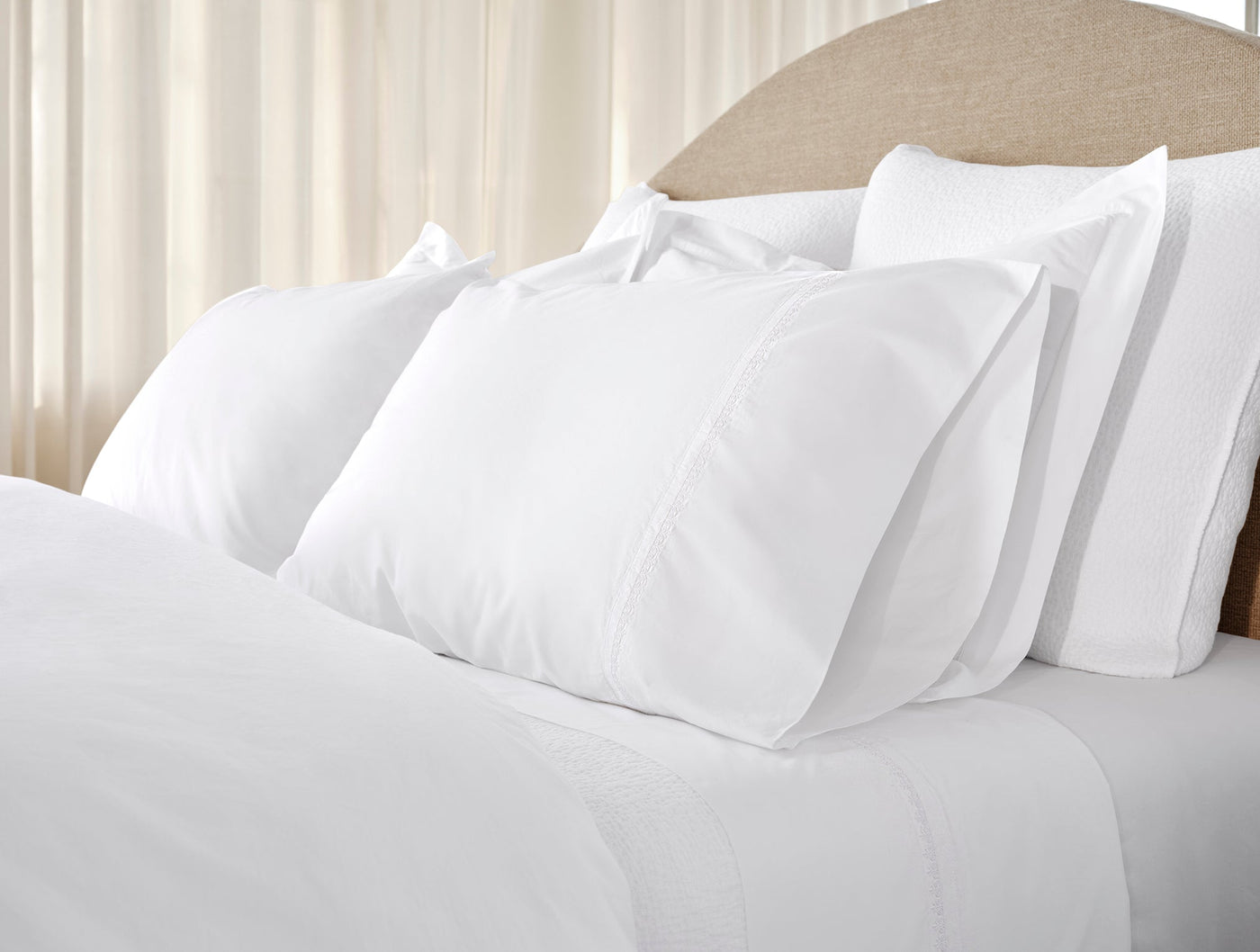 Four white pillows stacked on a made bed with crisp white sheets, soft natural light.