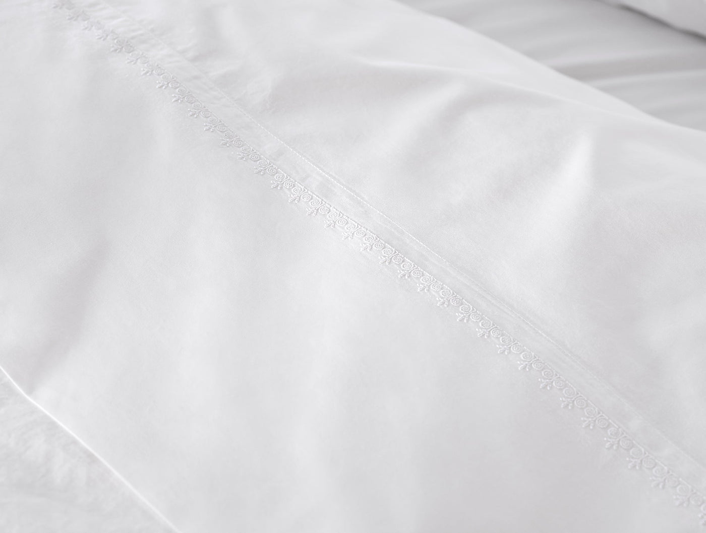 Close-up of delicate floral embroidered trim on white Coyuchi Floret sheet hem.