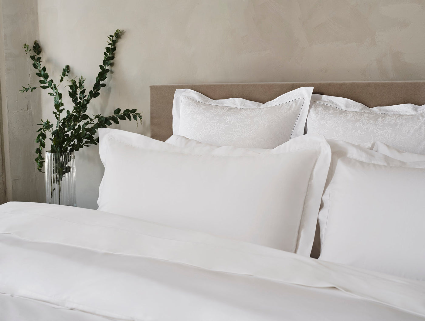 Coyuchi Heirloom Sateen sham in white, styled on a made bed with layered pillows.