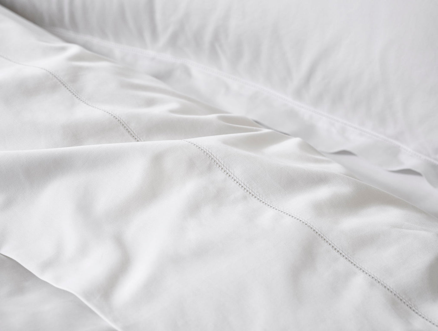Close-up of white sateen sheet hem with delicate hemstitch detail.