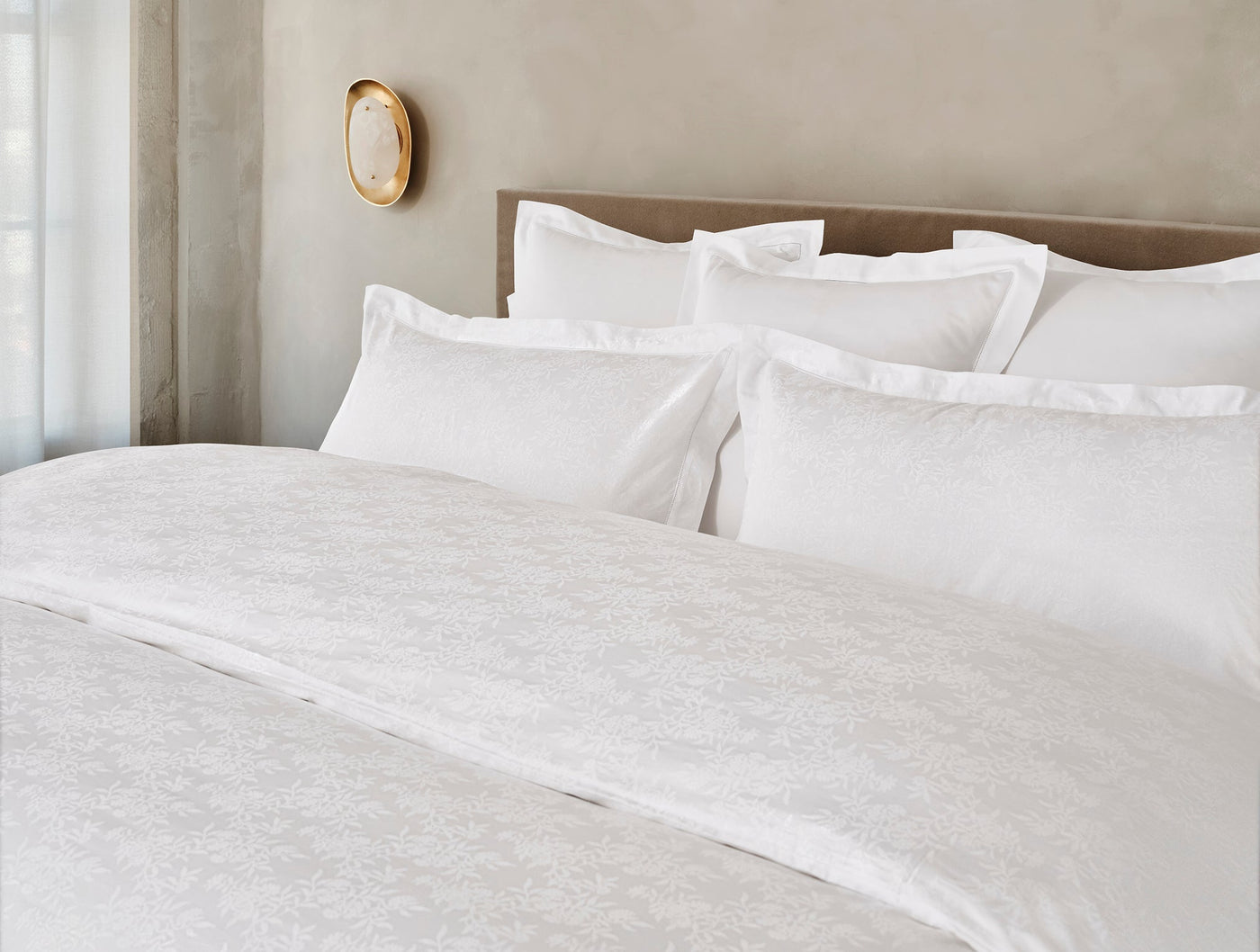 Ivory jacquard sham styled on a bed with white pillows, subtle woven floral pattern visible.