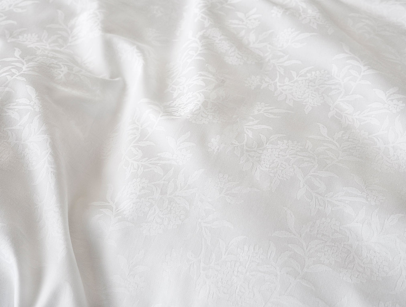 Close-up of white-on-white floral jacquard weave on draped Coyuchi Heirloom Sateen fabric.