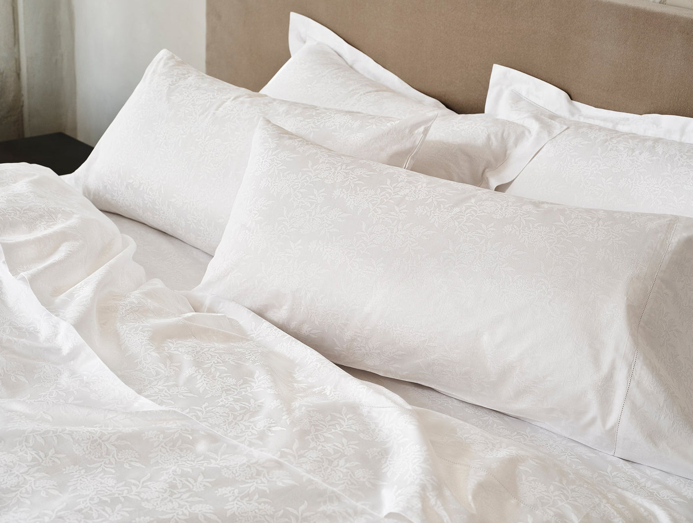White sateen jacquard sheet set styled on bed, floral tone-on-tone pattern visible across duvet and pillows.