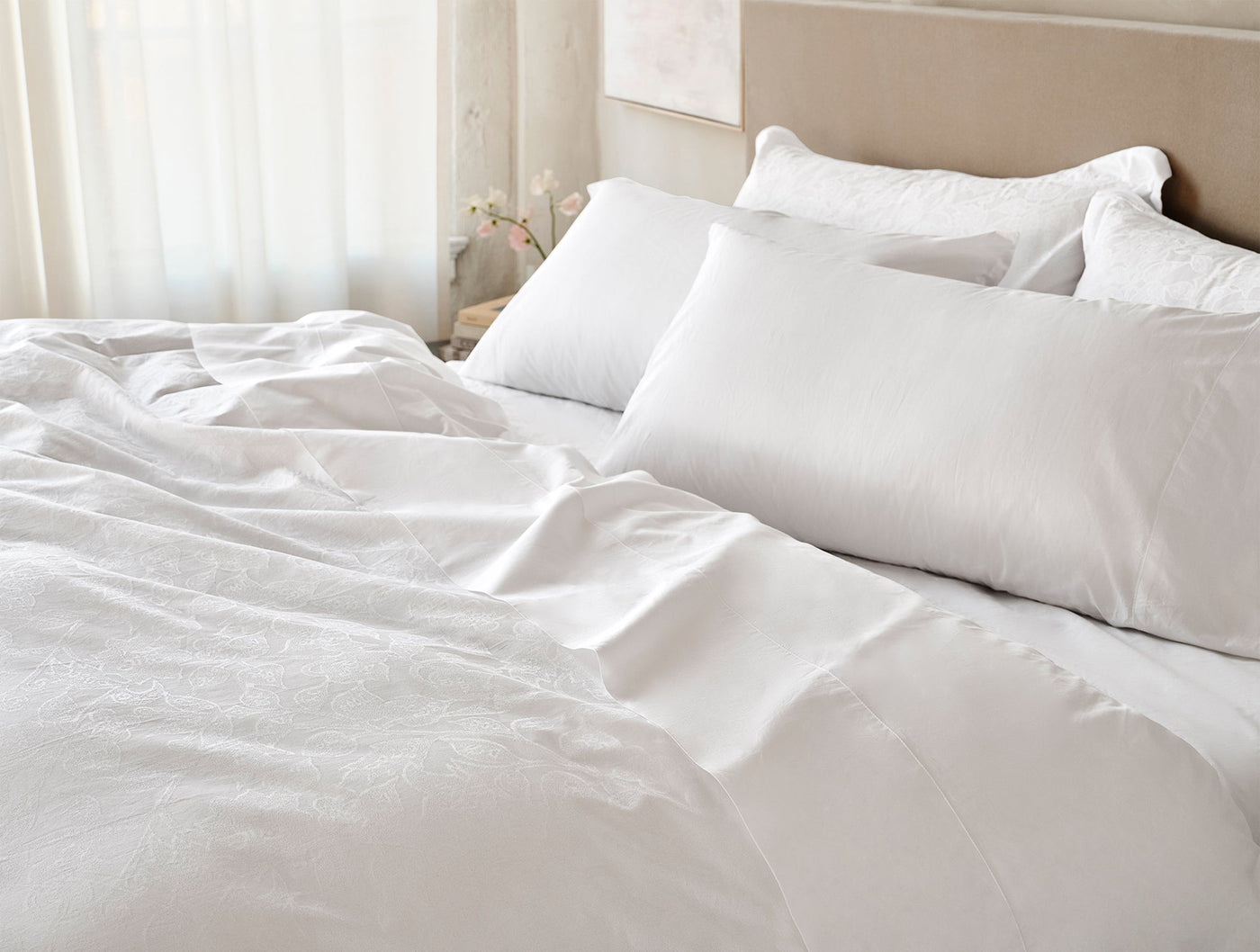 Rumpled white percale sheets and pillows on a sunlit bed, showing relaxed drape.