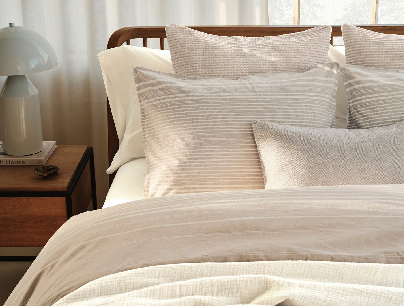 Layered ivory and sandy stripe bedding styled on a wood bed with sheer curtain backdrop.