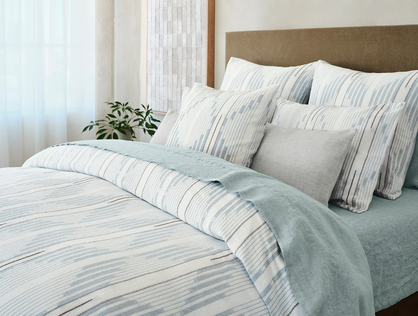 Close-up of Morelia sham styled on a bed with sage and ivory brushstroke stripe bedding.